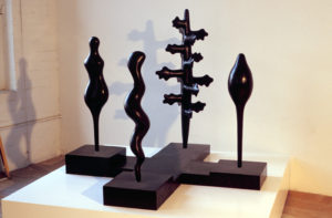 four suggestive elements including figures, a serpent, and a tree arranged on a geometric base in wax